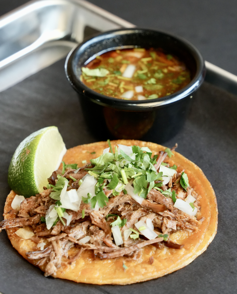 Señor Jalalpeño birria taco with shredded beef, onion, cilantro, lime and broth behind it