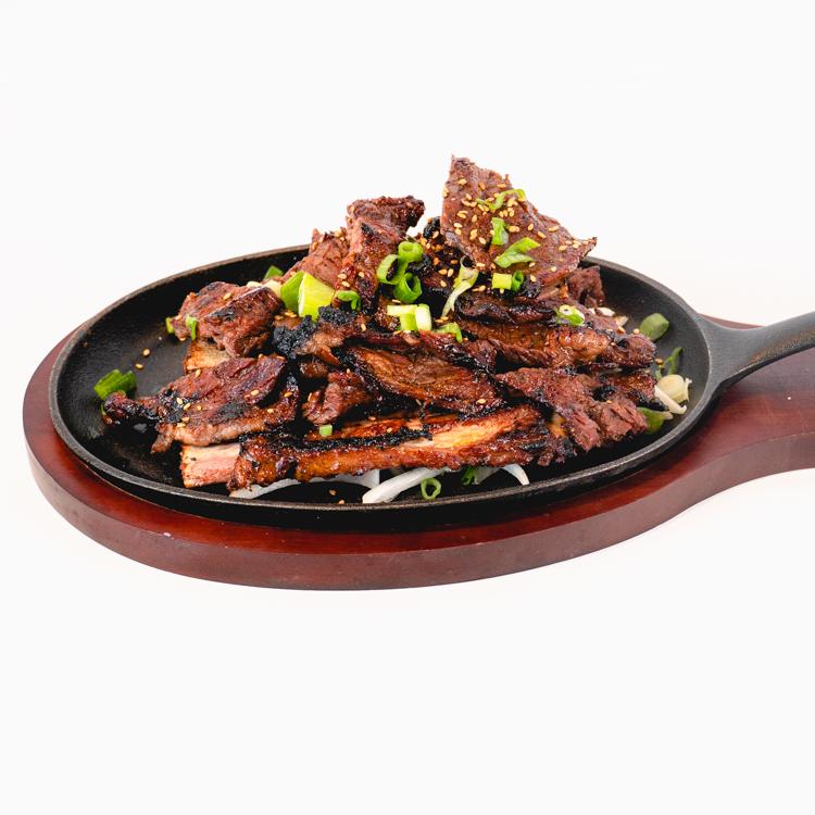 Seoul Bites kalbi: grilled bone-in beef short ribs with sesame and green onions on a black skillet