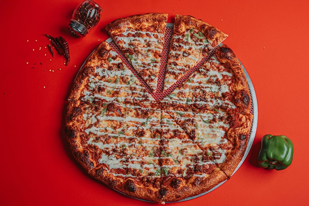 Slyce's The 53rd pizza with gyro meat, green peppers and white-sauce drizzle against a red background