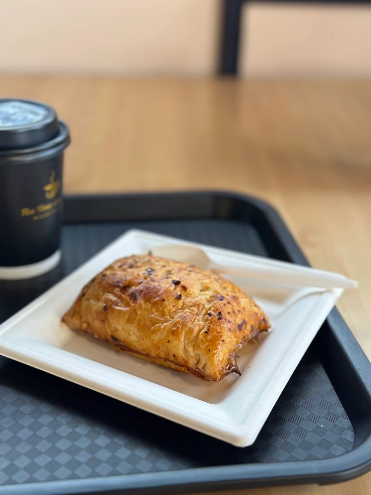 A golden puff pastry and branded TeaTime AnyTime hot-drink cup on a cafe tray