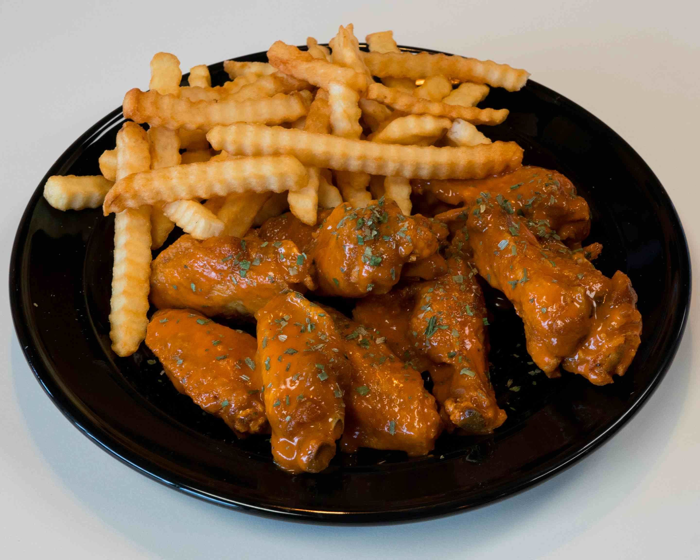 Sauced bone-in wings and crinkle-cut fries on a black plate at Wing Zing; sauce flavor unverified