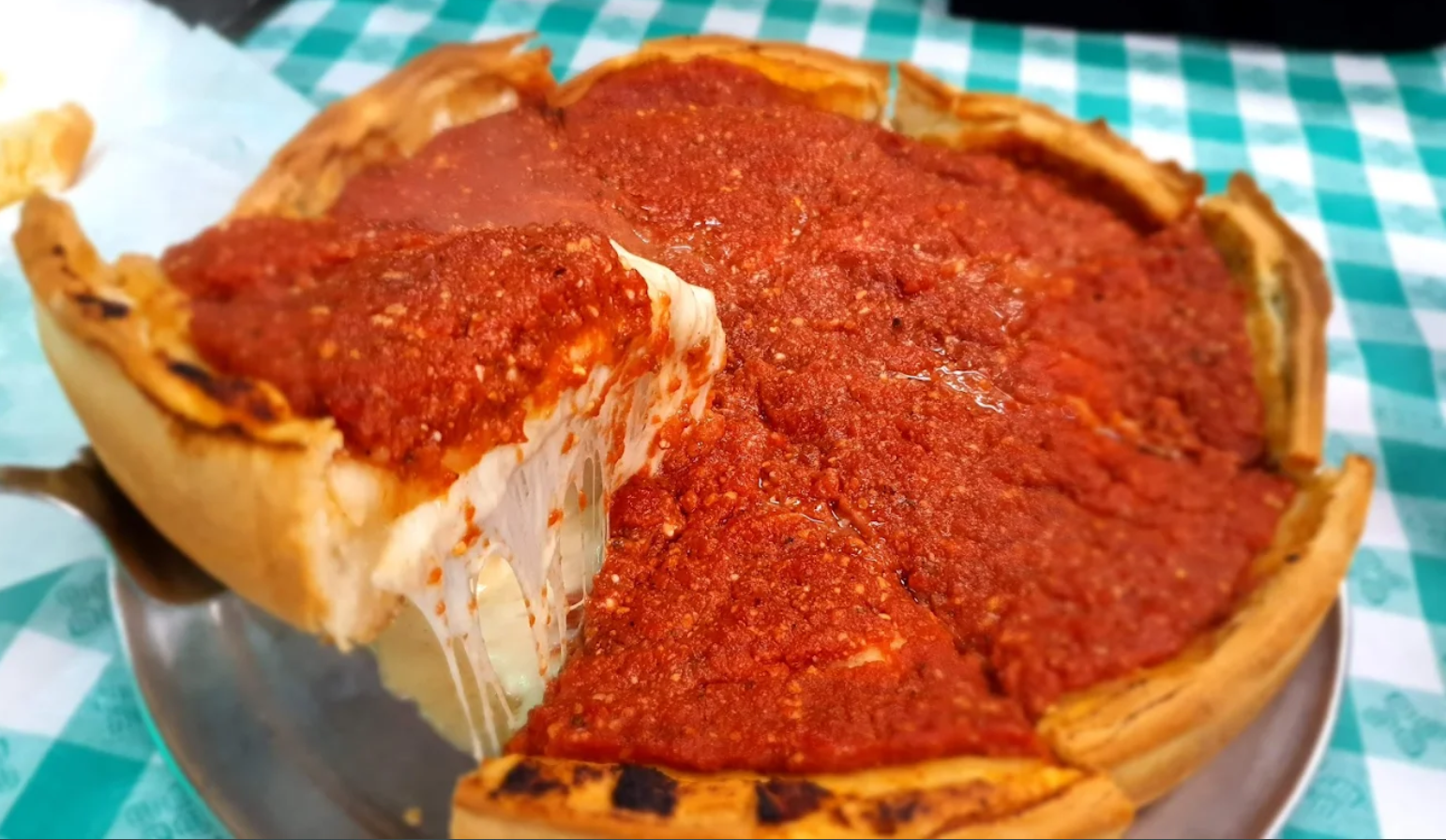 Zak's deep-dish pizza with tomato sauce, a lifted slice and melted cheese on a metal pan